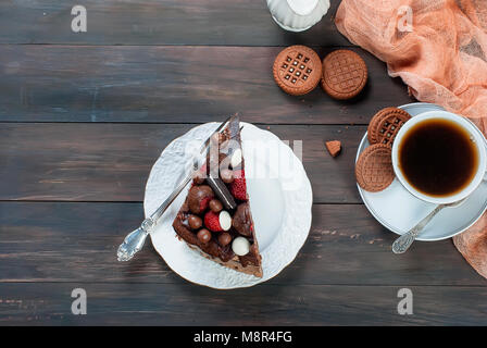 Morceau de gâteau au chocolat blanc sur assiette, tasse de café noir, jug et chocolat cookies sur la table en bois sombre arrière-plan. Vue du dessus avec spa de copie Banque D'Images