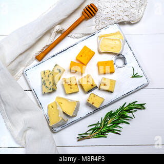 De petits morceaux de fromage brie, roquefort, camembert, cheddar et fromage aux noix sur une planche de bois blanc, Banque D'Images