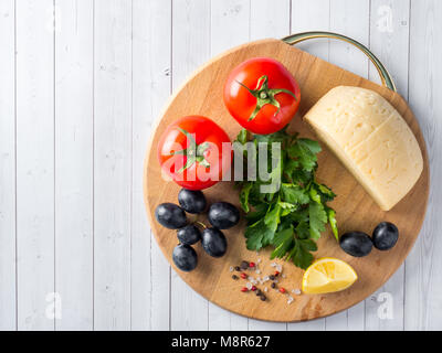 Morceau de fromage avec du persil, des tomates raisins sur une planche à découper Banque D'Images