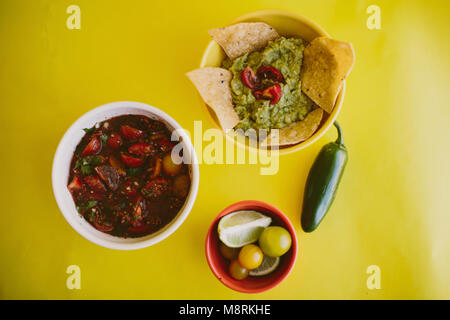 Close-up de la salsa et le guacamole servi avec des ingrédients sur fond jaune Banque D'Images