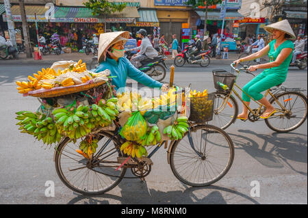 Rue du Vietnam, une femelle femme roues vendeur son vélo chargé de bananes le long de la route principale dans la région de Cholon Saigon, Ho Chi Minh City, Vietnam Banque D'Images