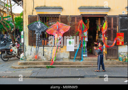 Vie de rue au Vietnam, vue d'un enfant vietnamien jouant avec un cerf-volant devant un magasin de cerf-volant coloré dans le quartier historique de la vieille ville de Hoi an, Vietnam. Banque D'Images