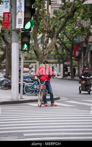 L'homme contrôle son téléphone portable pendant qu'il attendait avec son vélo pour traverser une route à Shanghai, Chine Banque D'Images