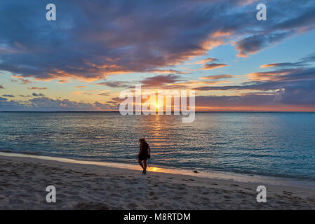 Une femme marchant le long de la plage du Morne à l'Île Maurice au coucher du soleil un soir d'été. Banque D'Images