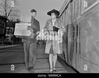 L'homme militaire transportant des colis et l'Escorte Femme à son domicile de l'arrêt de bus maintenant que la livraison des marchandises ont été réduites pour économiser sur les pneus et l'essence au cours de la Seconde Guerre mondiale, Ann Rosener pour Office of War Information, décembre 1942 Banque D'Images