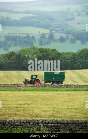 Tracteur vert avec remorque recueillaient de l'herbe pour l'ensilage, mais elles sont aujourd'hui garés en bordure du champ avec aucun pilote - West Yorkshire, Angleterre, Royaume-Uni Banque D'Images