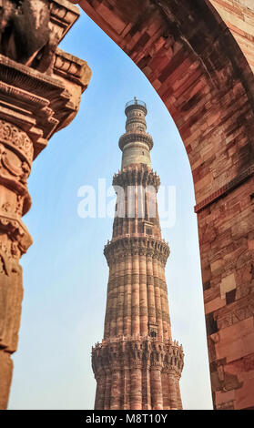 Qutub Minar minaret, partie de la complexe Qutab Minar, New Delhi, Inde. La tour de grès rouge encadrée par une voûte en pierre contre fond de ciel bleu Banque D'Images