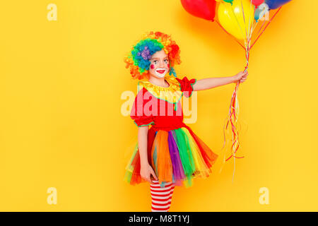 Clown Girl holding beaucoup de ballons se préparer pour partie. Studio shot, isolé sur fond jaune Banque D'Images