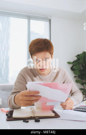 Jeune homme asiatique comptant à l'aide de la calculatrice et le stress en problème de dépenses. Banque D'Images