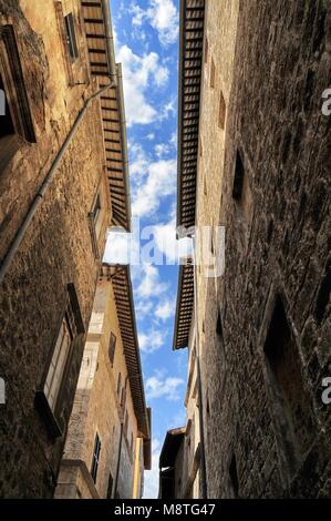 Ligne de ciel nuageux ciel bleu bitween ancienne en pierre biuldings dans une rue étroite de la cité médiévale vue du bas Ascoli Italie vers août 2015 Banque D'Images