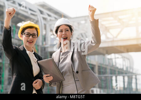 Deux jeunes asiatiques femmes architectes de célébrer avec un grand sourire joyeux et à l'avant. L'une des femmes tenant une tablette sur la main. Banque D'Images