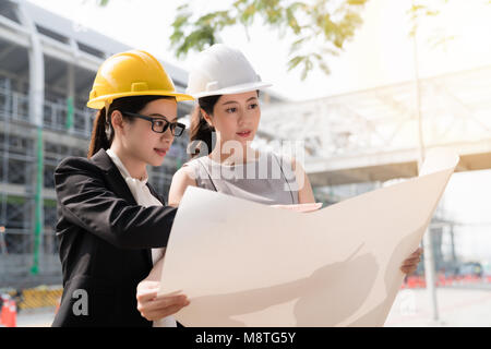 Deux architecte asiatique girl wearing helmat regardant le plan de bâtiment. Sur un chantier de construction. Banque D'Images