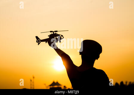 Silhouette Garçon jouant modèle d'hélicoptère avec du soleil. Banque D'Images