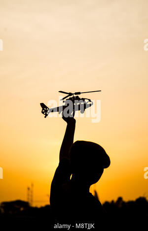 Silhouette Garçon jouant modèle d'hélicoptère avec du soleil. Banque D'Images