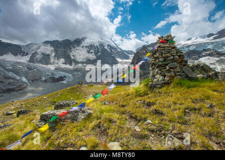 Vue magnifique sur le Mont Cervin et le glacier, Alpes Suisses. Randonneur grimpe à la piste Marqueur, pile de roche et de drapeaux de prière Tibetains. La neige, la glace, les nuages. Banque D'Images