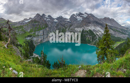 Grande vue panoramique depuis un surplomb d'Oeschinen lake, lac glaciaire dans les Alpes suisses. Cirque de montagnes, plage, forêt d'herbe et les arbres, nuages dans le ciel. Banque D'Images