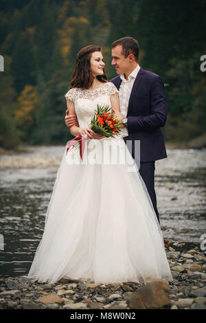 Élégant élégant happy brunette mariée et le marié magnifique sur l'arrière-plan d'une belle rivière dans les montagnes Banque D'Images