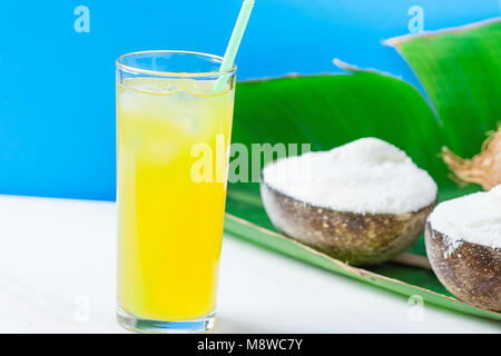 Glace Coco Vegan délicieux dans des bols sur de grandes feuilles de palmiers verts avec verre de jus de fruits tropicaux sur table en marbre blanc fond bleu. En fonction de l'usine Banque D'Images