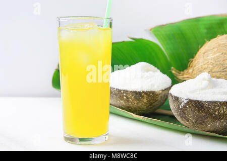 Glace Coco Vegan délicieux dans des bols sur de grandes feuilles de palmiers verts avec verre de jus de fruits tropicaux sur table de marbre blanc. Régime alimentaire à base de plantes Vac d'été Banque D'Images