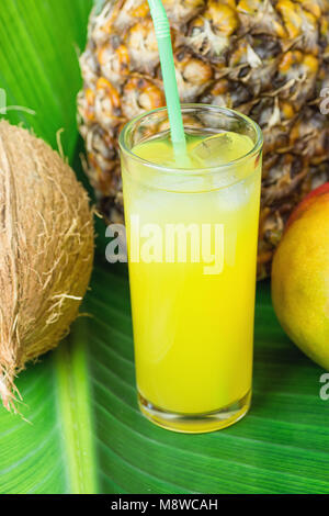 Composition Grand Verre à jus de fruits tropicaux fraîchement pressé avec de la paille de coco ananas mangue sur grande feuille de palmier vert. La lumière du soleil. Summer Vacati Banque D'Images