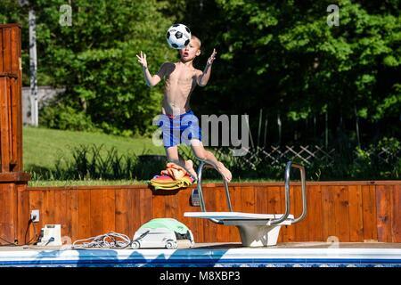 Jeune garçon de sauter dans la piscine et attraper une balle Banque D'Images