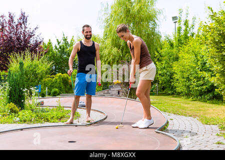 Couple jouant ensemble miniature golf outdoors Banque D'Images