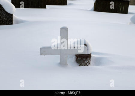 Cimetière en hiver, une petite croix en bois et une lanterne couverte de neige Banque D'Images