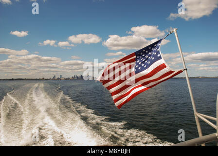 Les Stars and Stripes drapeau des États-Unis d'Amérique aux commandes de l'arrière d'un traversier rapide avec le Boston skyline en arrière-plan Banque D'Images