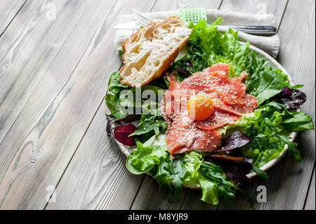 Salade de saumon fumé, oeuf, salade fraîche, feuilles de roquette, épinards et pousses de betteraves dans une assiette sur un fond de bois. Vue d'en haut Banque D'Images