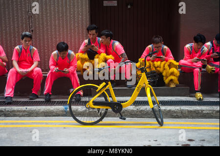 28.02.2018, Singapour, République de Singapour, en Asie - les membres d'un groupe de danse du lion reste au bord de la route dans le centre de Singapour et de jouer aux jeux vidéo. Banque D'Images
