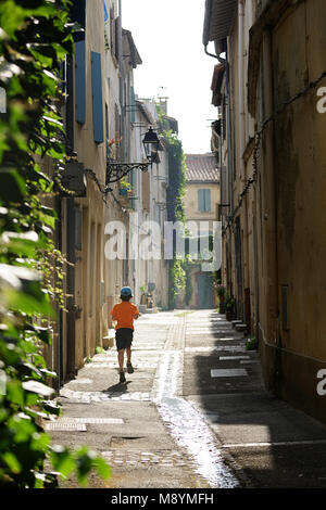 Jeune garçon en orange tshirt et bouchon bleu en marche à travers les rues d'Arles, scène de rue à Arles, Provence, France Banque D'Images