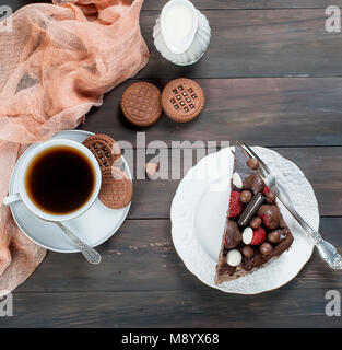 Morceau de gâteau au chocolat blanc sur assiette, tasse de café noir, jug et chocolat cookies sur la table en bois sombre arrière-plan. Vue du dessus avec spa de copie Banque D'Images