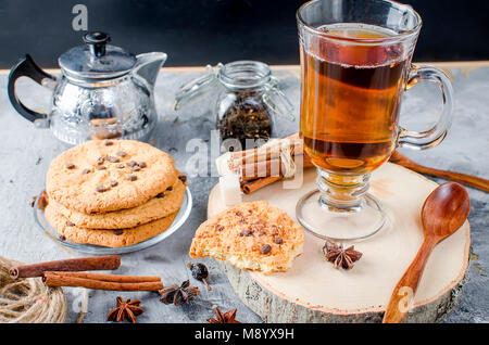 Pile de biscuits maison сup avec pastilles de chocolat, de thé noir chaud, la cannelle, l'anis sur fond sombre, les épices pour le thé. Banque D'Images