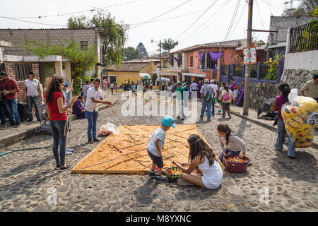 Antigua, Guatemala : le 18 mars 2018 : la famille travaillant sur alfombres, tapis faits par la sciure de couleur sur les rues pavées pour la procession San Bartolo Banque D'Images