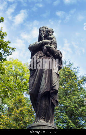 Ancienne statue de la Vierge Marie avec l'enfant Jésus Christ contre le ciel bleu. La sculpture sur pierre de la Mère de Dieu sur l'ancien cimetière Banque D'Images