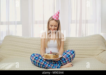 Une fille blonde dans un bouchon de pyjama avec un gâteau avec une bougie célébrat Banque D'Images