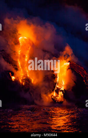 L'eau de mer et la roche en fusion splatter ensemble juste avant le lever du soleil comme une vague s'écrase sur la lave pahoehoe découlant de Kilauea dans l'océan Pacifique n Banque D'Images