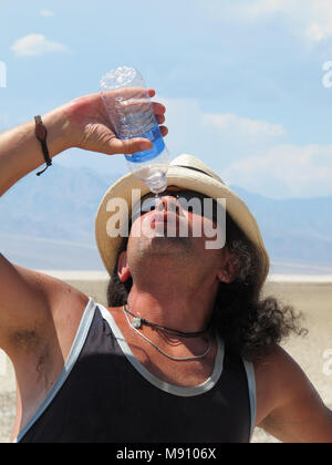 Guy déshydraté dans le désert goulument boit de l'eau. Bassin de Badwater à Death Valley NP. California-Nevada, USA. Banque D'Images
