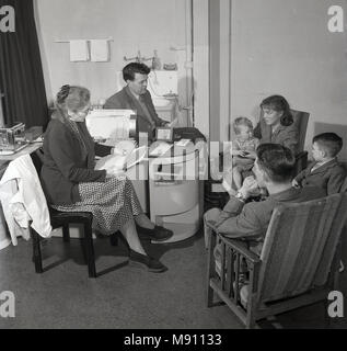 Années 1950, photo historique.. santé.. un jeune couple avec leurs deux enfants assis ayant une discussion ou consultation avec leur médecin local ou GP, England, UK. Banque D'Images