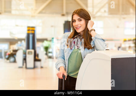 Jeune femme avec sac chariot en utilisant l'auto check-in à l'aéroport. Banque D'Images