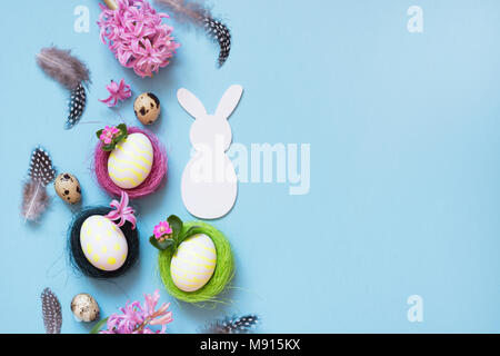 Concept de Pâques. Lapin blanc et les oeufs de poule peint avec décor de fleurs roses sur fond bleu. Vue d'en haut. Mise à plat. Banque D'Images