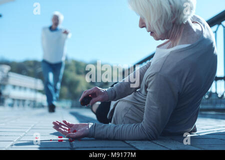 Femme couchée sur le trottoir prendre des pilules pour la douleur de secours Banque D'Images