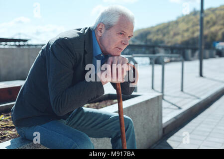 Vue latérale sur l'homme triste avec la canne à la vacance en Banque D'Images