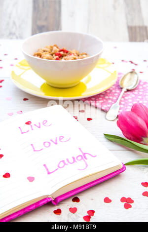 Un ordinateur portable rose avec une citation inspirante disant vivre, aimer, rire dans-le sur une table de petit-déjeuner féminin top au petit-déjeuner. Banque D'Images