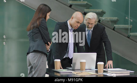Les gens de l'entreprise multi-ethnique en discutant affaires réunion du bureau à l'aide d'un ordinateur portable dans un bureau moderne. Banque D'Images