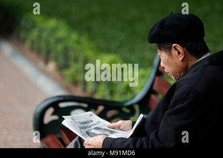 Vieux homme vietnamien assis sur un banc avec du papier journal. Hanoi. Le Vietnam. Banque D'Images