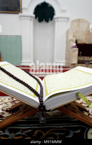 Un Coran et une prière musulmane des perles sur stand en bois avec mihrab en arrière-plan. Banque D'Images