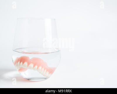 Une prothèse acrylique immergé dans un verre d'eau fond blanc Banque D'Images