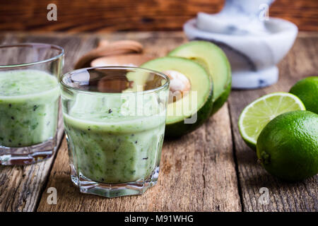 Cyril Lignac smoothie légumes vert style dans les verres avec des ingrédients de l'avocat et lime sur table en bois rustique, salé boisson laitière saine avec org Banque D'Images