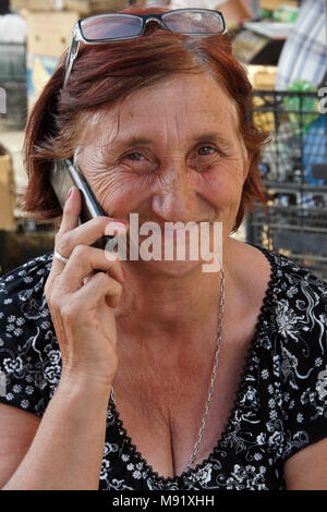 Une femme plus âgée avec hennaed et verres de cheveux sur le dessus de sa tête à l'aide d'un téléphone mobile à l'Dezerters' Bazar marché en plein-air, Tbilissi, Géorgie Banque D'Images